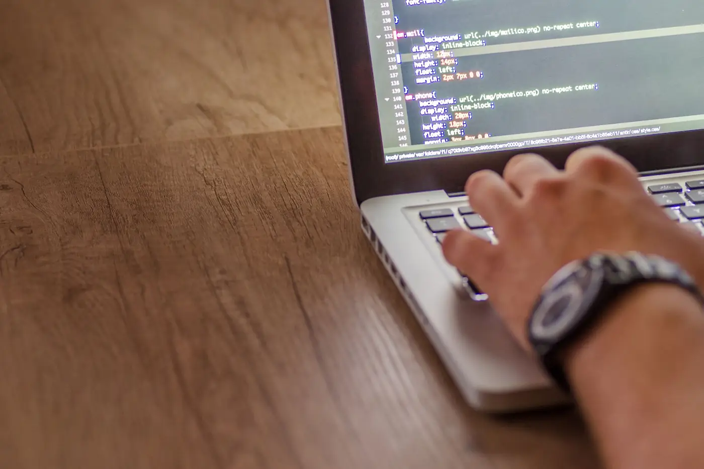 Hands typing code on a laptop at a wooden desk