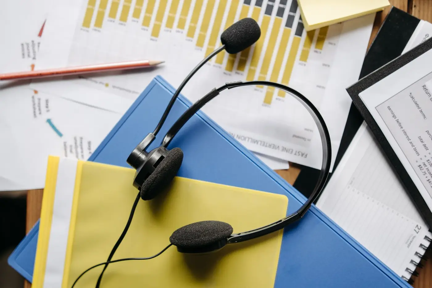 A headset resting on charts and folders on an office desk